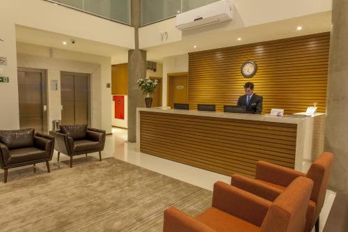 a man standing at a reception desk in a lobby at São Carlos Marklin Suítes in São Carlos