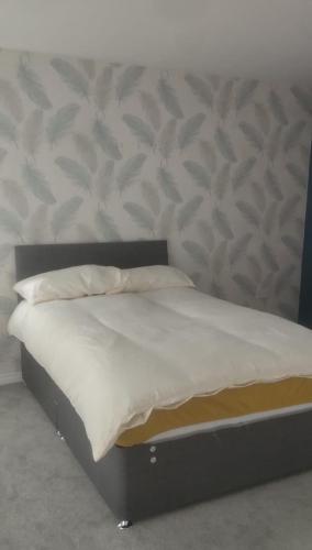 a bed with white sheets and a headboard with a wall at Telford Guest House 1 in Telford