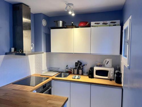 eine Küche mit weißen Schränken und einer Mikrowelle in der Unterkunft Appartement charmant bord de mer in Cabourg