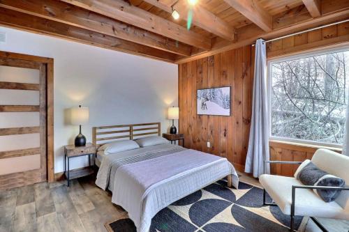 1 dormitorio con 1 cama, 1 silla y 1 ventana en Chalet Jumeaux Mont Édouard Ski & Nature en LʼAnse-Saint-Jean