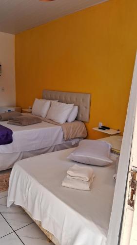 two beds in a room with a yellow wall at Pousada Alforria in Lavras Novas