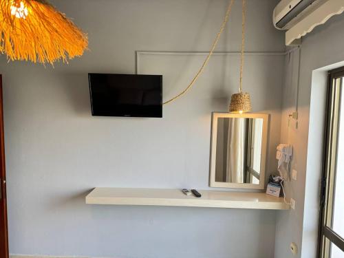 a tv on a wall with a shelf and a mirror at The 3 Little Pigs apartments in Sidari