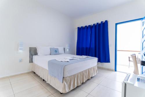a white bedroom with a large bed with blue curtains at La Suite Praia Hotel in Caucaia