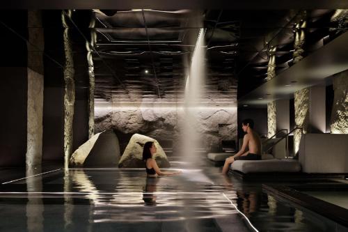 a man and woman sitting in a swimming pool with a waterfall at HOTEL THE MITSUI KYOTO, a Luxury Collection Hotel & Spa in Kyoto