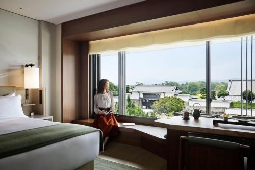 a woman looking out of a window in a hotel room at HOTEL THE MITSUI KYOTO, a Luxury Collection Hotel & Spa in Kyoto
