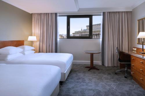 リバプールにあるDelta Hotels by Marriott Liverpool City Centreのベッド2台、デスク、窓が備わるホテルルームです。