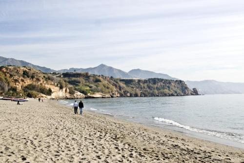 people walking on a beach with mountains in the background at Apartamentos HC Burriana Playa in Nerja