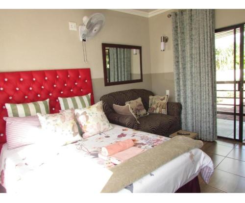 a bedroom with a bed with a red headboard and a couch at BelaBela Guesthouse in Bela-Bela
