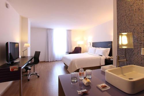 メキシコシティにあるフィエスタ イン ナウカルパンのベッドとデスクが備わるホテルルームです。