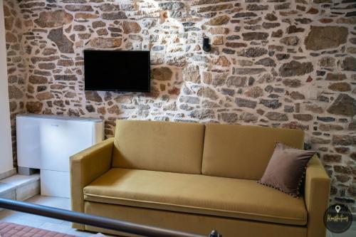 a couch in front of a stone wall with a tv at SKINOS rooms and apartment in Pyrgi