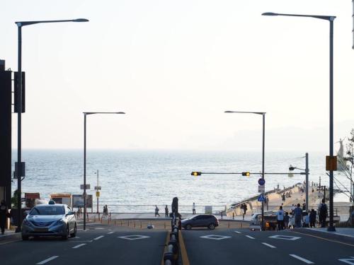 a street with cars driving down a road next to the ocean at Haeundae Mipo House22 in Busan