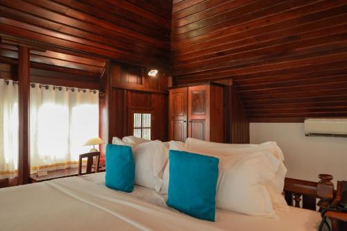 a bedroom with a large bed with blue pillows at Coconut Lagoon Kumarakom- a CGH Earth Experience in Kumarakom