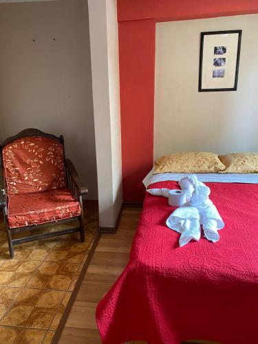 un osito de peluche sentado en una cama roja con una silla en Rosita´s House Huaraz, en Huaraz