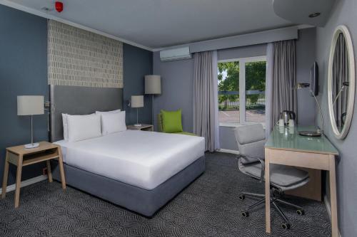 a hotel room with a bed and a desk and a bed and a chair at Holiday Inn Johannesburg OR Tambo Airport Hotel by IHG in Kempton Park