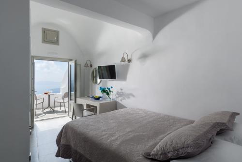 a white bedroom with a bed and a balcony at Krokos Villas in Imerovigli