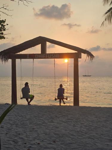 two people sitting on swings on the beach at sunset at Nirili Villa in Dhiffushi