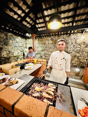 a man standing in a kitchen preparing food on a grill at Colonial Retreat Villa in Talawatugoda