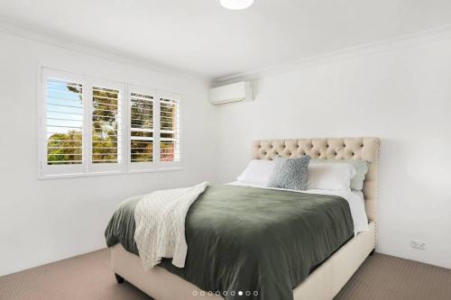 a white bedroom with a bed and two windows at Stylish Beachside Sanctuary, steps to the beach in Sydney