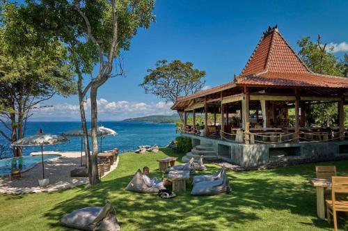 a building with people sitting on the grass near the water at Bali Cliff Glamping in Karangasem