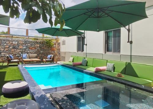 a swimming pool with a green couch and two umbrellas at Villa Salvia - Country style luxury & a captivating poolscape in Áyiai Paraskiaí