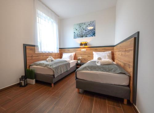 two beds in a bedroom with wooden floors and a window at Silver Home Apartman "A" in Balatonalmádi