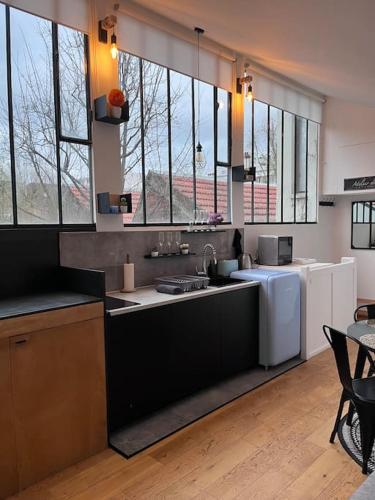 eine Küche mit einer Spüle, einem Kühlschrank und Fenstern in der Unterkunft Loft chic climatisé proche château de Vincennes in Montreuil
