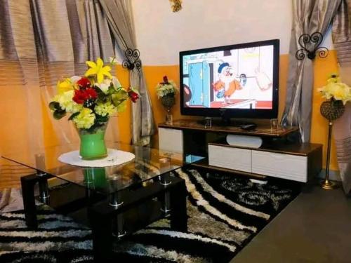 ein Wohnzimmer mit einem TV und Blumen auf dem Tisch in der Unterkunft STUDIO MEUBLE in Douala