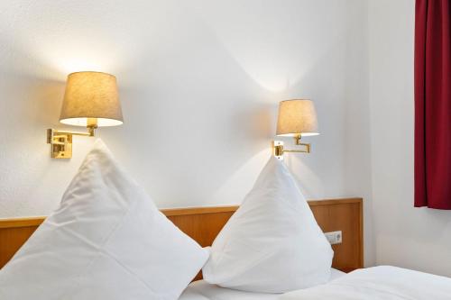 two pillows on a bed with two lamps on the wall at Hotel Garni Traube in Friedrichshafen