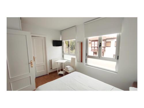 a white bedroom with a bed and two windows at Pension Villa ** in Comillas
