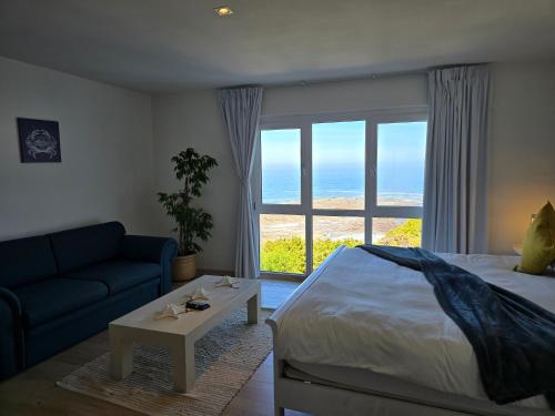 a bedroom with a bed and a couch and a window at Swept Away B&B - No-Loadshedding in Yzerfontein