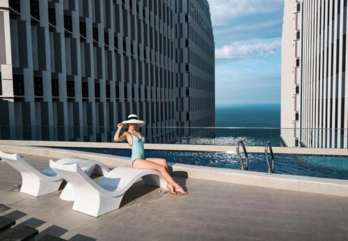 a woman sitting on a bench next to a pool at Apec Mandala Chambay Mũi Né in Phan Thiet