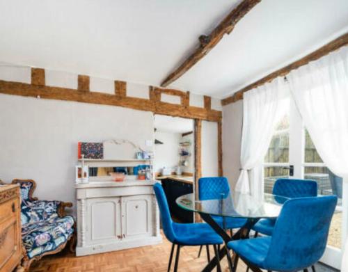 uma sala de jantar com uma mesa de vidro e cadeiras azuis em Little Mouse Cottage em Lavenham