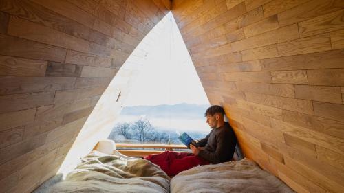 a man sitting on a bed reading a book in a window at ALPS LAPS withTENAR in Kami-iino