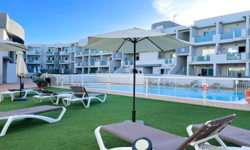 a pool with chairs and an umbrella next to a building at Paradise Palms I Deluxe, incl. Welcome Package in Corralejo