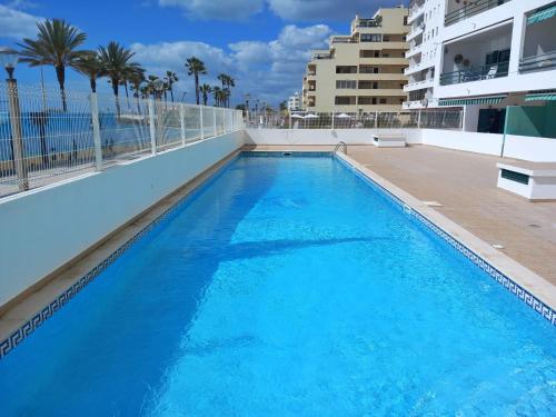 a large blue swimming pool with palm trees and buildings at Beachfront flat with pool in Quarteira