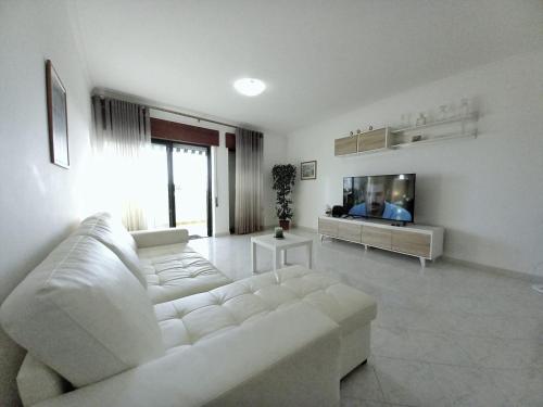 a living room with a white couch and a tv at Beachfront flat with pool in Quarteira