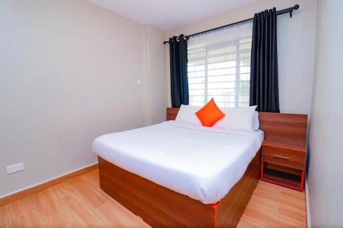 een slaapkamer met een bed met een oranje kussen en een raam bij 1 Bedroom near TRM gate C in Nairobi