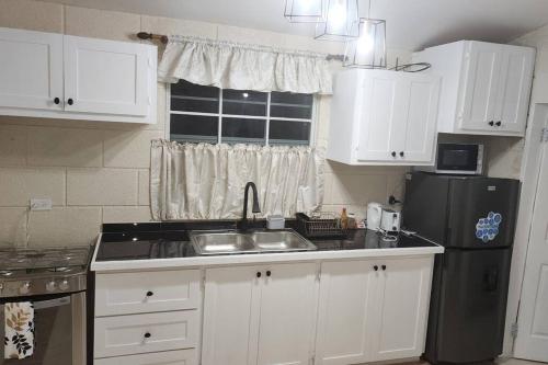 a kitchen with white cabinets and a sink and a refrigerator at Welcome to our 1 bedroom villa in Bridgetown