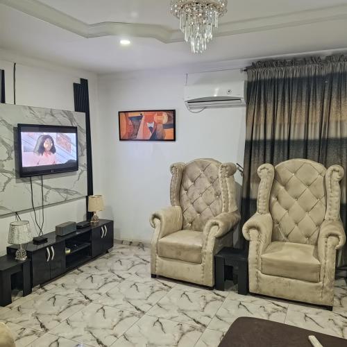 J Lounge في Ikorodu: غرفة معيشة مع كرسيين وتلفزيون