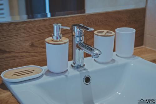 a bathroom sink with a faucet and cups on it at Kompleks Tawerna Vito - Apartamenty Vito in Czorsztyn
