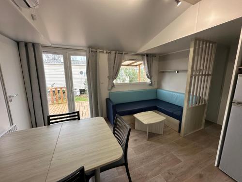 un salon avec une table et un canapé bleu dans l'établissement Mobil-home - Narbonne-Plage - Clim, TV, à Narbonne-Plage