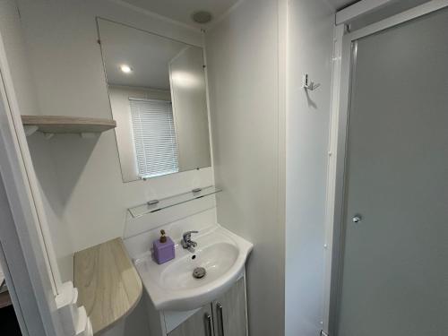 une salle de bain blanche avec un lavabo et un miroir dans l'établissement Mobil-home - Narbonne-Plage - Clim, TV, à Narbonne-Plage