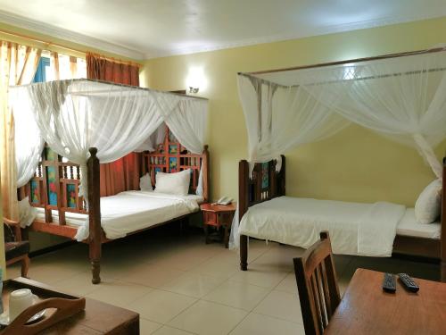 una camera con 2 letti a baldacchino, un tavolo e un mobile da bagno con lavabo. di New Safari Hotel 