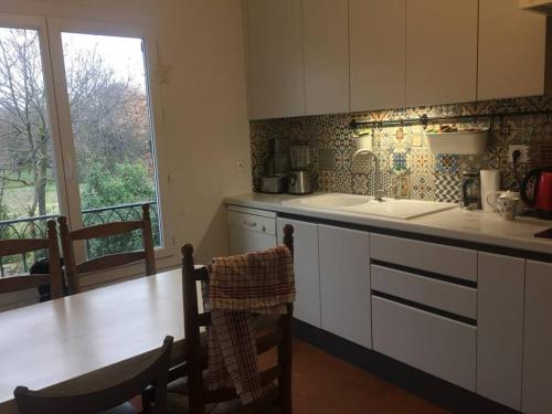 une cuisine avec des armoires blanches, une table et une fenêtre dans l'établissement Agréable Maison 4 chambres wifi et parking gratuit, à Montpellier