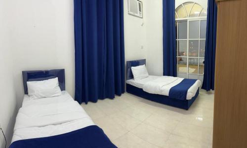 2 letti in una camera con tende blu e finestra di Al Manafa Furnished Apartments a Salalah