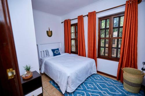 a bedroom with a bed and windows with orange curtains at Peaceful and Cozy Home in Arusha in Ngateu