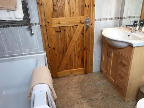 a bathroom with a wooden door and a tub and sink at Penlan Coastal Cottages in Aberporth