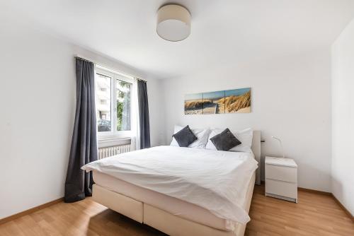 a white bedroom with a bed and a window at Cooldis G in Kreuzlingen