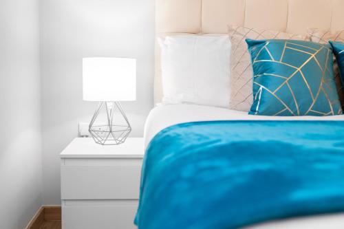 Modern 2 Bedroom Apartment - Off-street Parking - Top Rated - 1aS : سرير مع بطانية زرقاء ومصباح على كومودينو