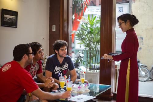 a woman talking to a group of people at a table at La Storia Ruby Hotel & Travel in Hanoi